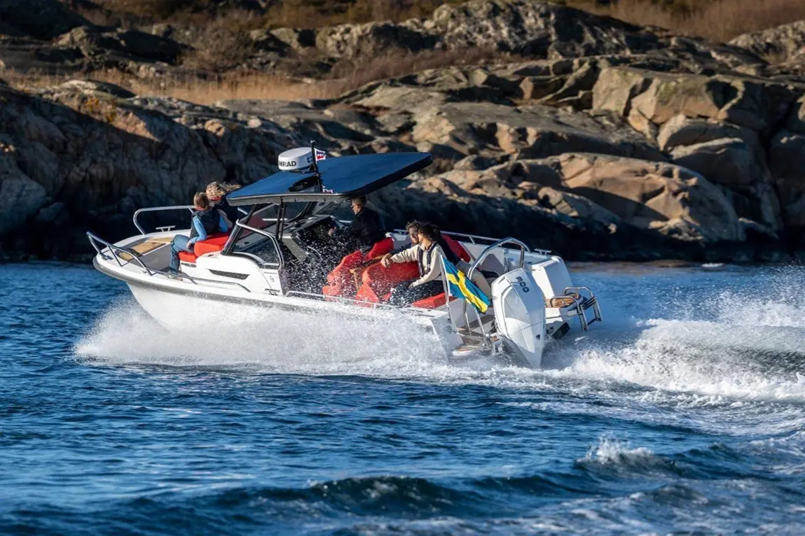 A motorboat speeds over water, with four people on board enjoying the ride, rocky coastline in the background.